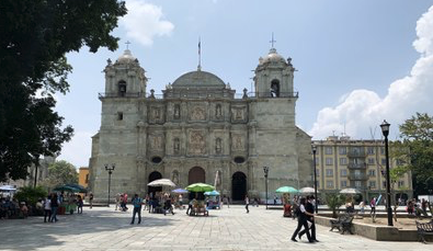 A outdoor scenery of people walking and a historic architectural building in Mexico in the background. 